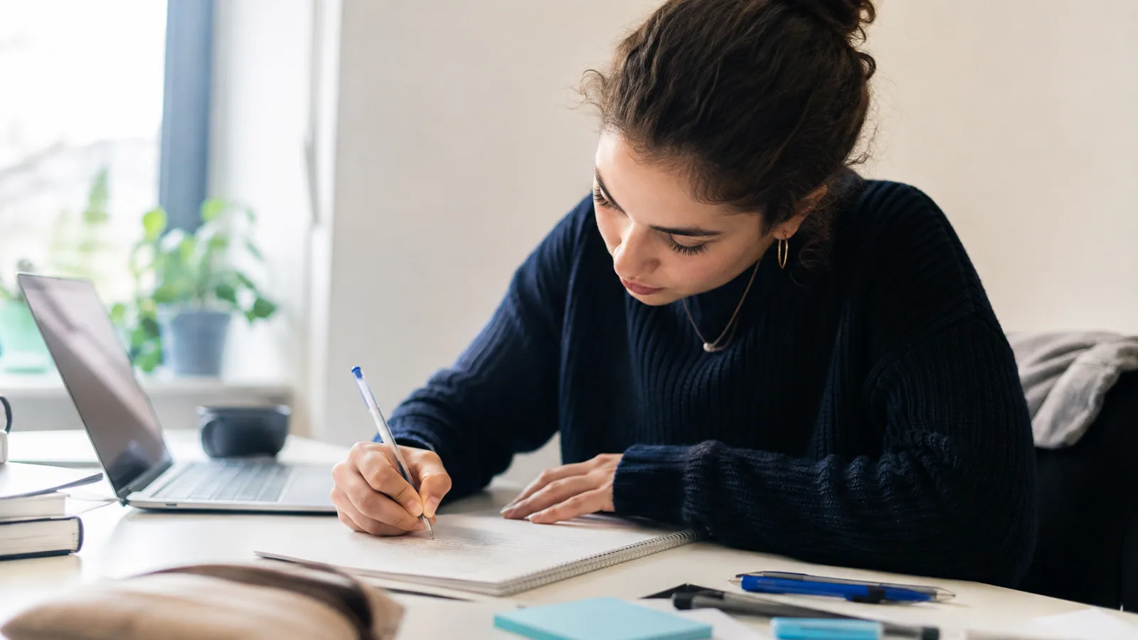 Studentin bearbeitet eine Aufgabe mit Stift und Notizheft.