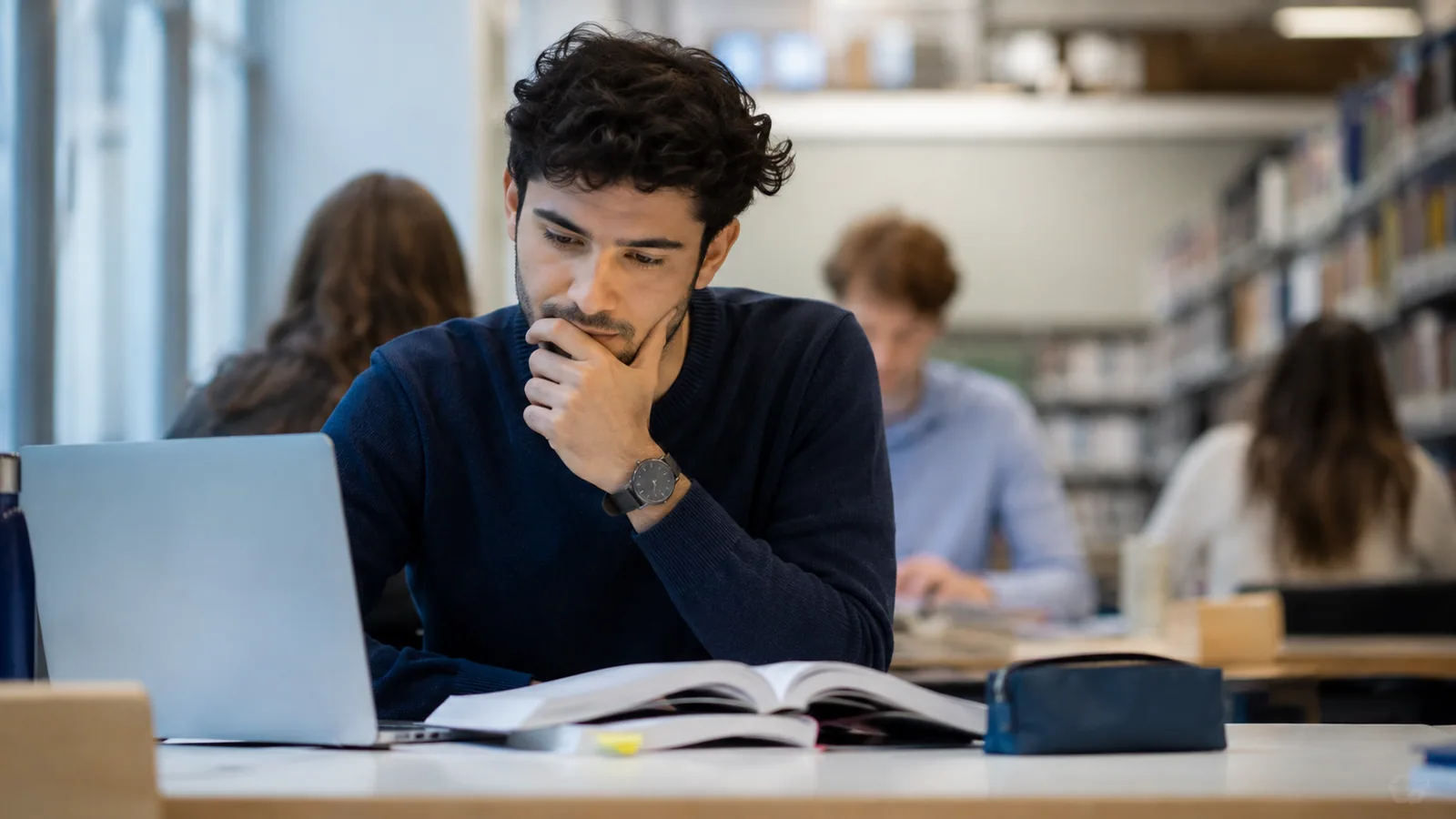 Student denkt in einer Bibliothek über eine Aufgabe nach.